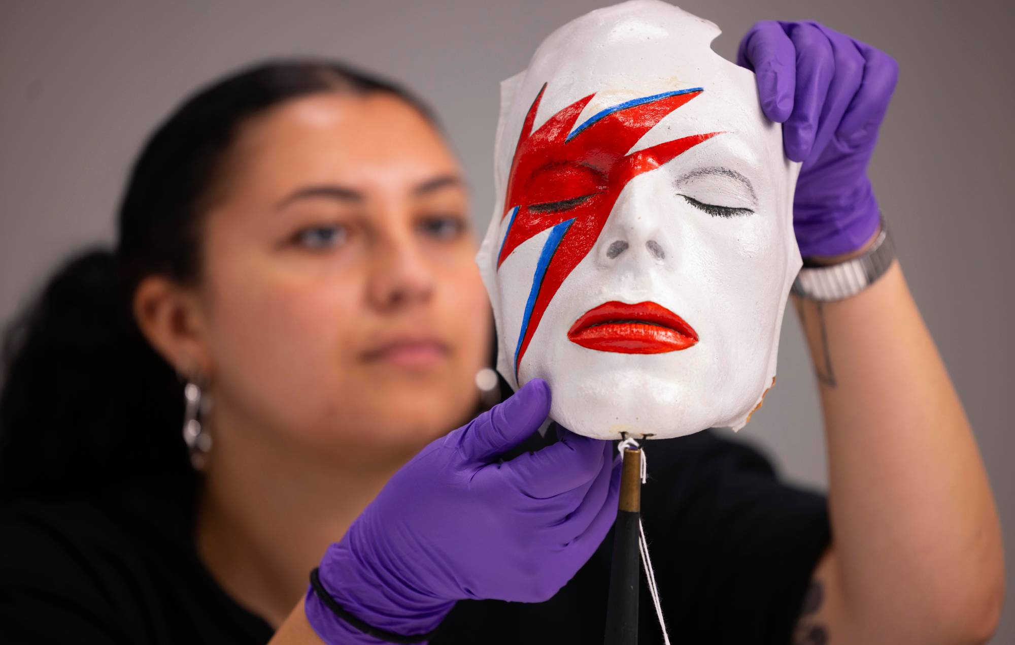 A V&A Collections Access Officer handles a life mask by William Forsche of David Bowie’s face painted to resemble his makeup from Aladdin Sane. Credit: David Parry for the V&A